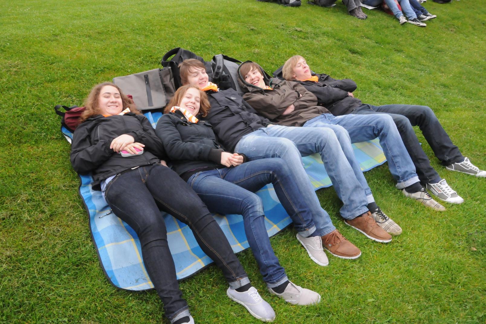 Jugendlche liegen gemeinsam auf Matten auf dem Boden und freuen sich